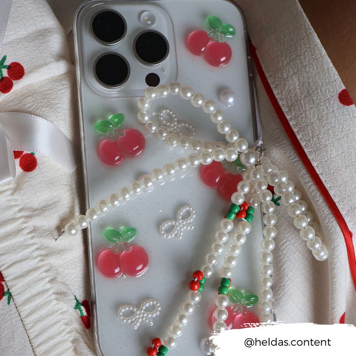 Coconut Lane phone case with cherry and bow pattern, pearl beaded strap, and cherry-print fabric detail.