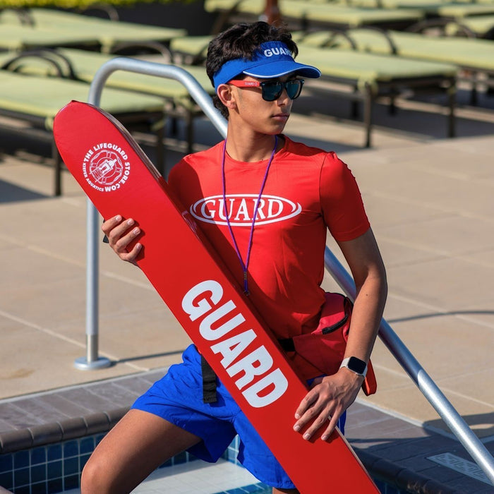 The Lifeguard Store red 50" vinyl rescue tube with "GUARD" lettering, held by a lifeguard.