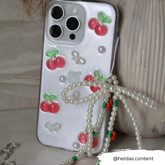Coconut Lane phone case with cherry and bow pattern and a pearl beaded charm on a textured surface.