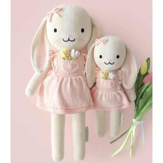 Two knitted bunny dolls in pink dresses on a light pink background with tulips.