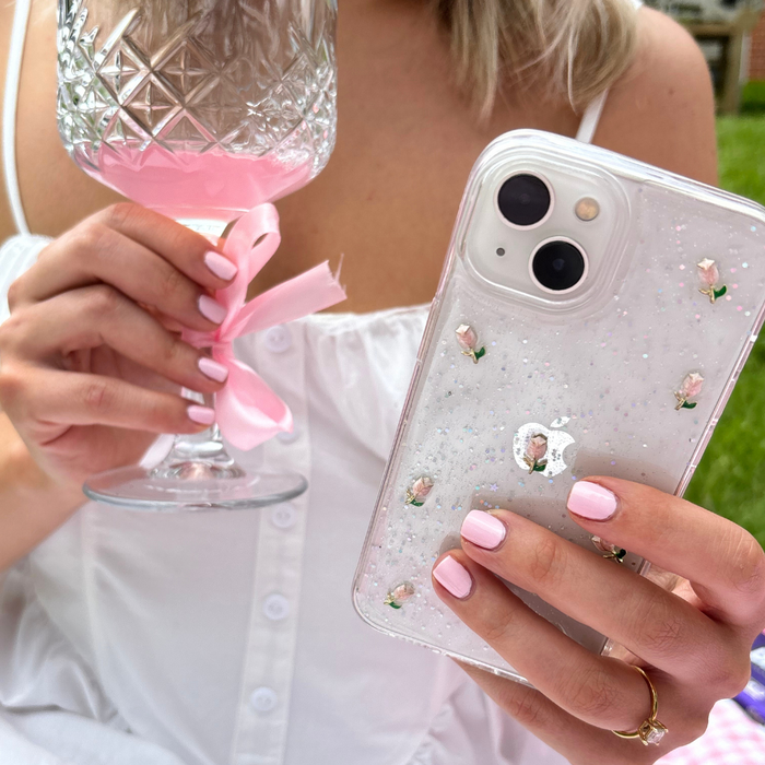 Woman in white dress holds iPhone 15 with Coconut Lane clear phone case featuring a tulip pattern; nails are light pink.