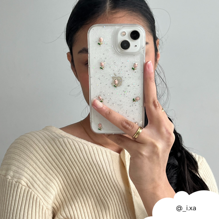Woman with dark hair holds a clear phone case with a tulip pattern; wearing a cream sweater and gold ring.