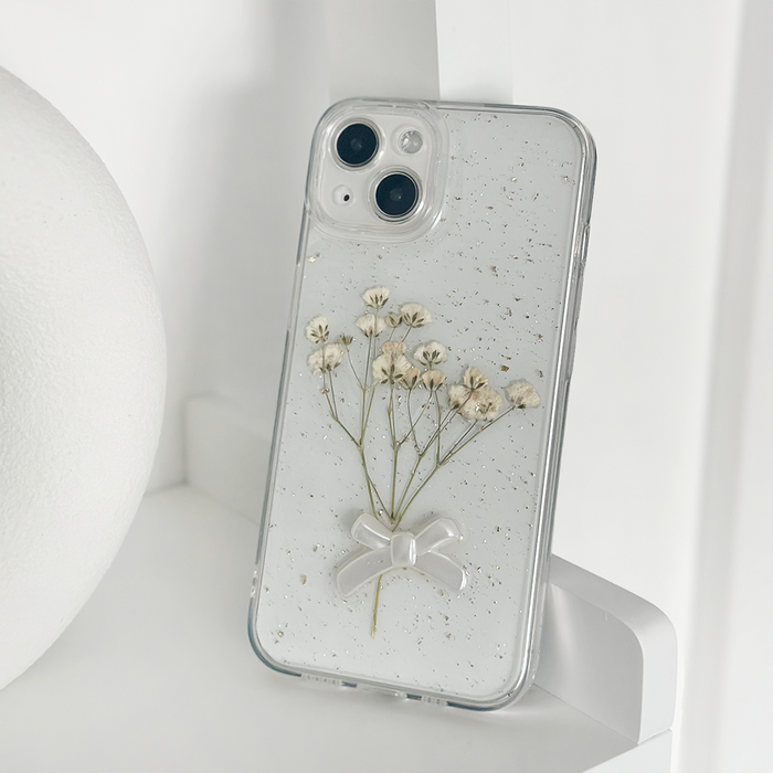 Clear phone case with white dried flowers and a bow, displayed on a white shelf.
