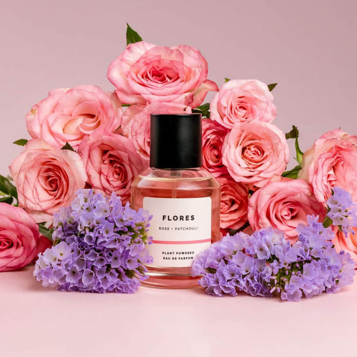 Perfume bottle labeled 'ECO. Modern Essentials Flores plant-powered eau de parfum' surrounded by pink & purple flowers on a pink background.