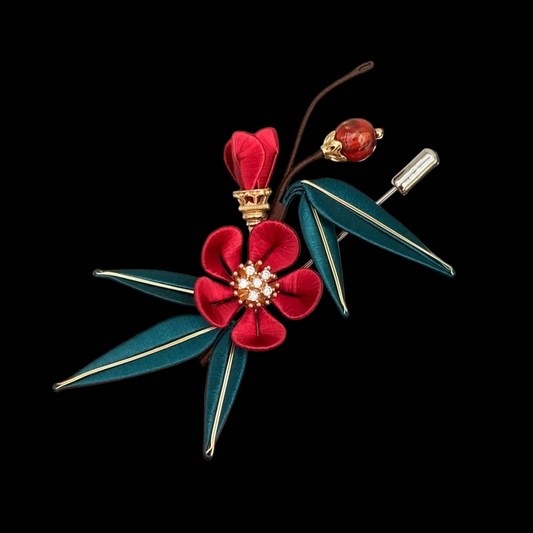 Close-up of Chanhua plum blossom brooch showing thread-wrapped red petals, crystal stamen cluster, and teal bamboo leaf detail with gold trim