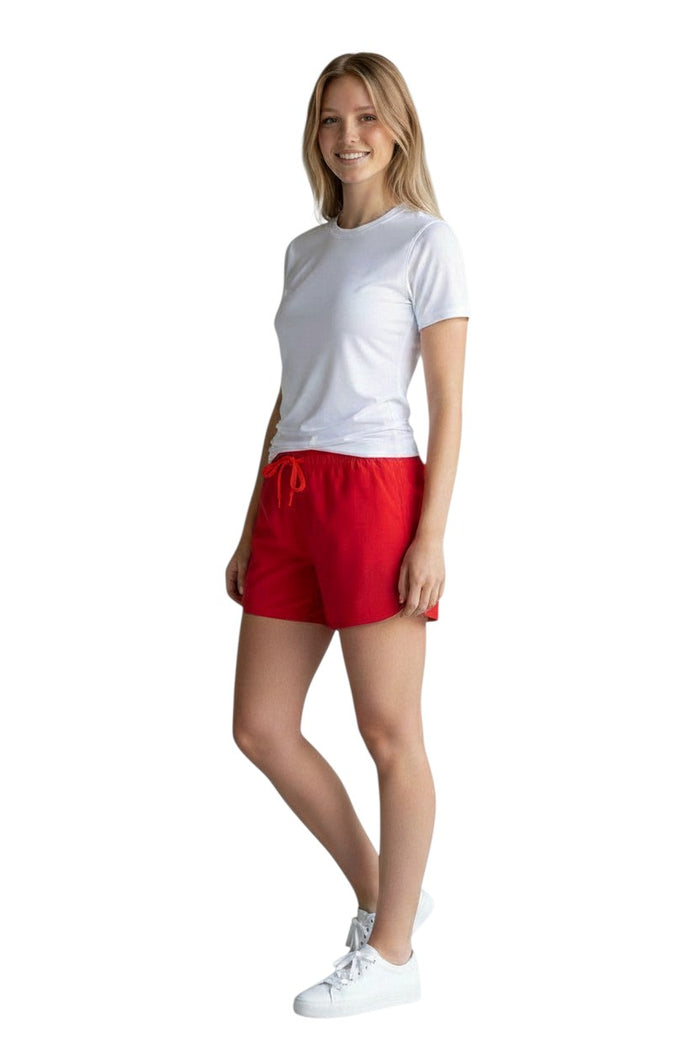 The Lifeguard Store Kiefer Women’s 5” red quick-dry shorts with drawstring and side pockets. Model is wearing a white t-shirt and sneakers.
