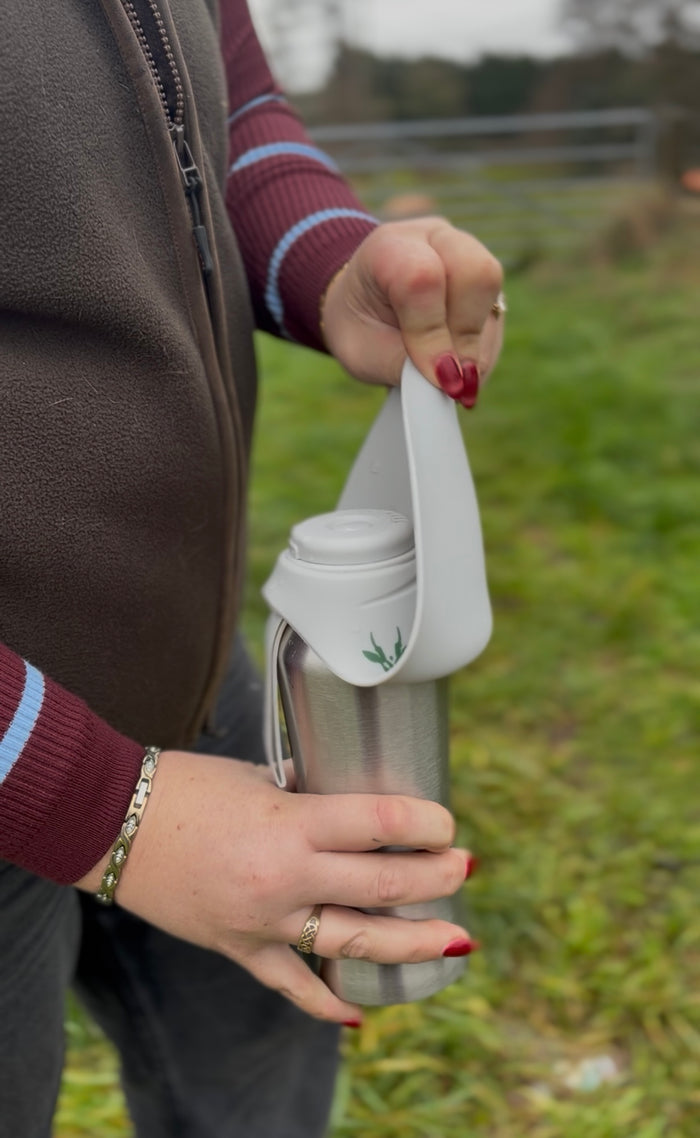 Person holding a thermos with a strap in an outdoor setting