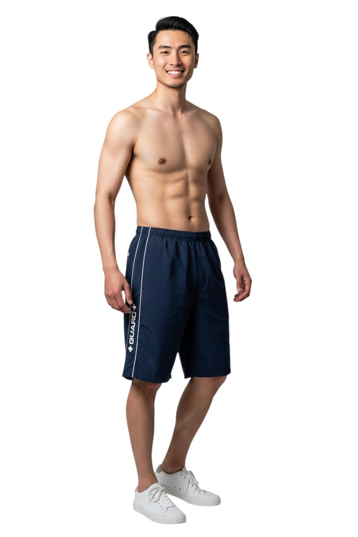 The Lifeguard Store RISE Guard Flex Short in navy blue polyester with white contrast piping and "GUARD+" logo. Features elastic waistband and side pocket.