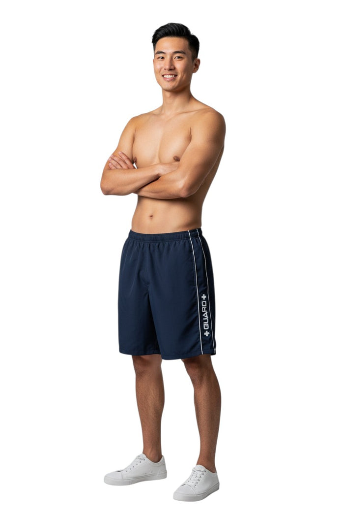 The Lifeguard Store RISE Guard Flex Short, navy blue polyester-spandex blend boardshorts with white contrast piping and "GUARD+" logo.