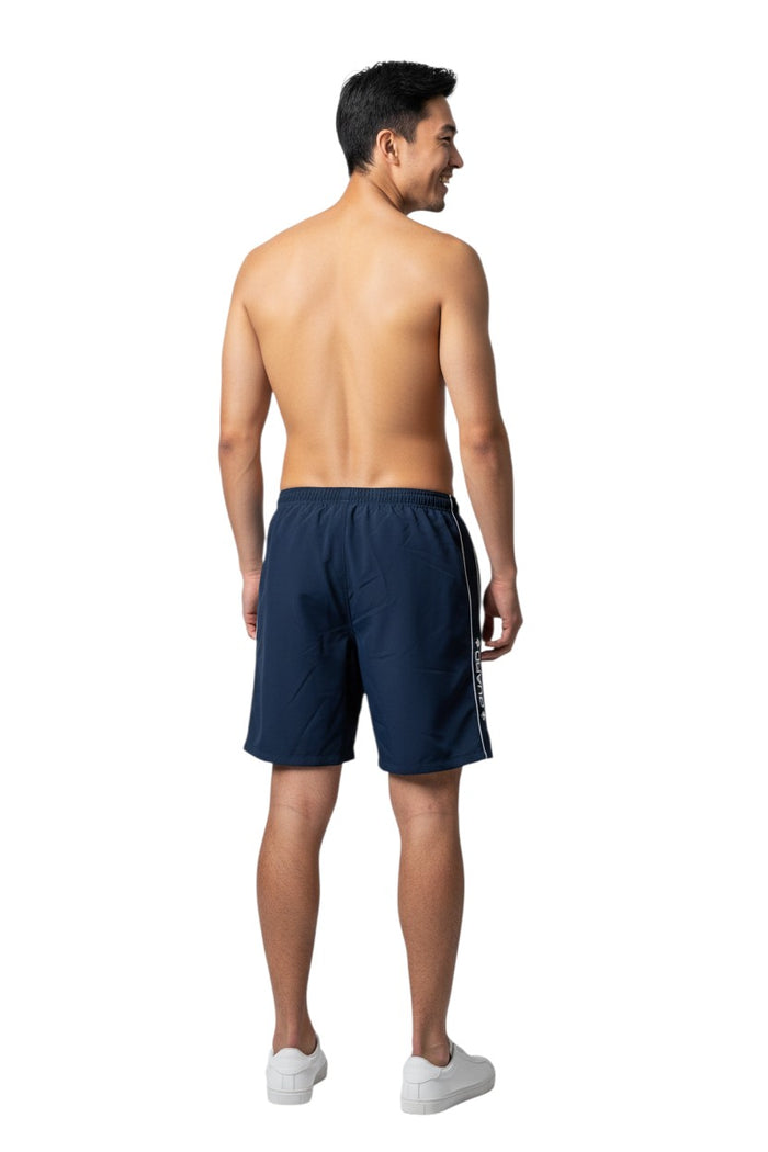 The Lifeguard Store RISE Guard Flex Short in navy blue polyester with white contrast piping and "GUARD+" logo. Features elastic waistband and side pocket.