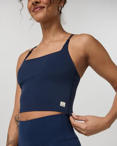 Woman wearing a navy blue Vuori - AllTheFeels Strappy Back top and leggings on a light gray background