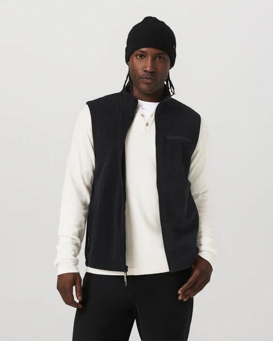 Person wearing a black Vuori Aspen Vest over a white shirt with a plain background