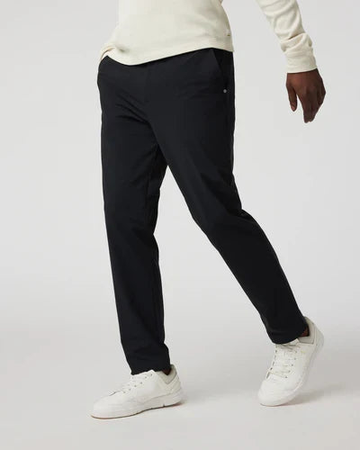 A person wearing black Vuori - Fleet Chino Pant Athletic Slim 30" pants and a white top, standing against a white background.
