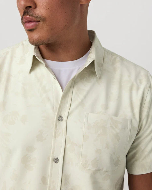 Man wearing a light beige Vuori short-sleeve shirt over a white t-shirt against a plain background