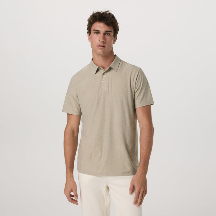 Man wearing a Vuori - Strato Tech Poloand white pants on a light gray background