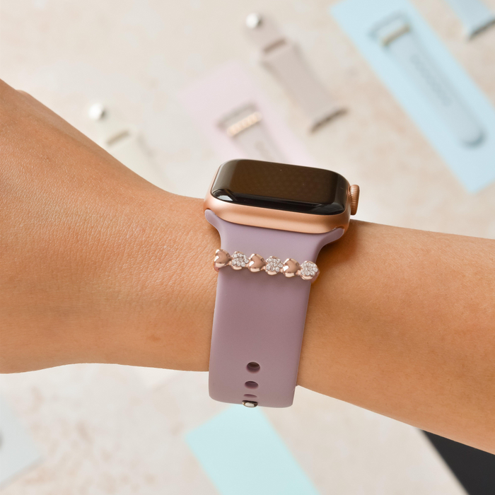 Lavender-banded smartwatch with a rose gold diamante heart charm, shown with extra bands in the background.