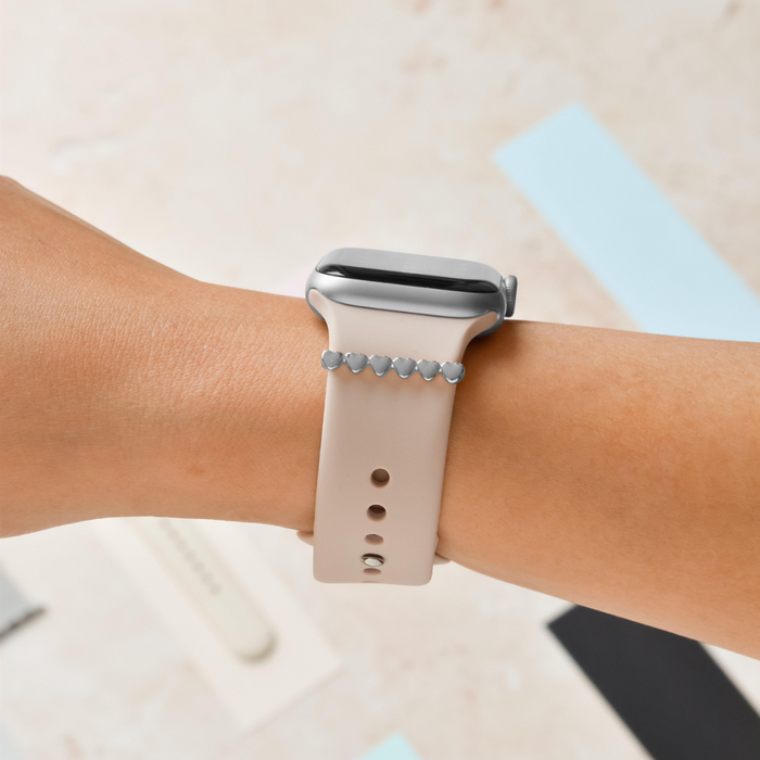 Silver heart watch strap charm by Coconut Lane on a beige smartwatch band, shown worn on a wrist.