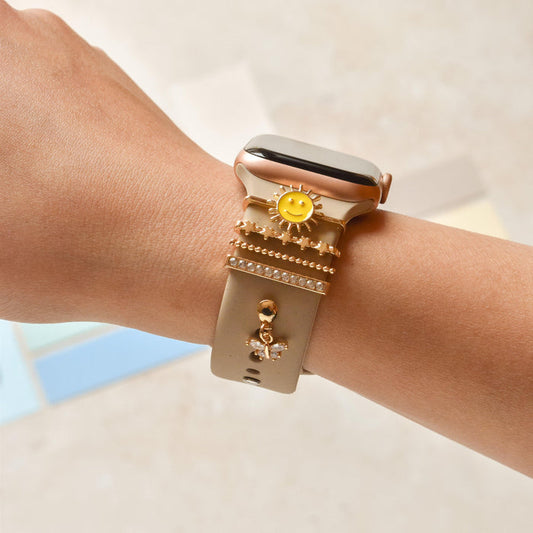 Gold Smiley Sun charm from Coconut Lane attached to a smartwatch band, shown on a persons wrist.