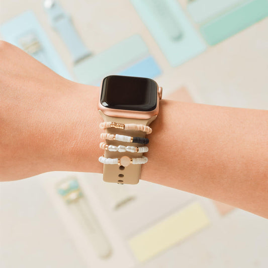Nude & Chic Coconut Lane watch strap charm pack on a smartwatch, with colorful strap accessories in the background.